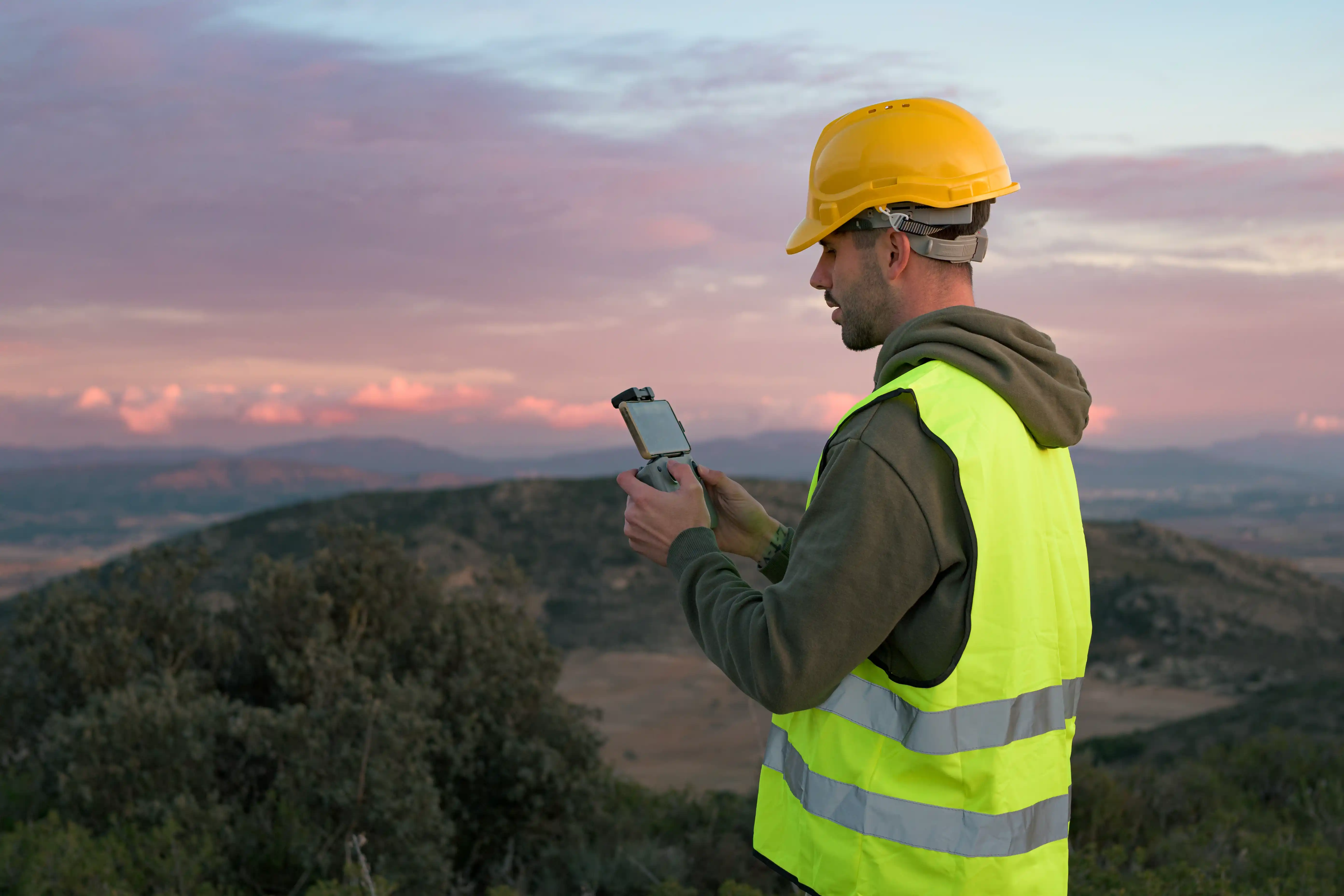 Field worker in hard hat and hi-vis vest using a mobile device on a job site